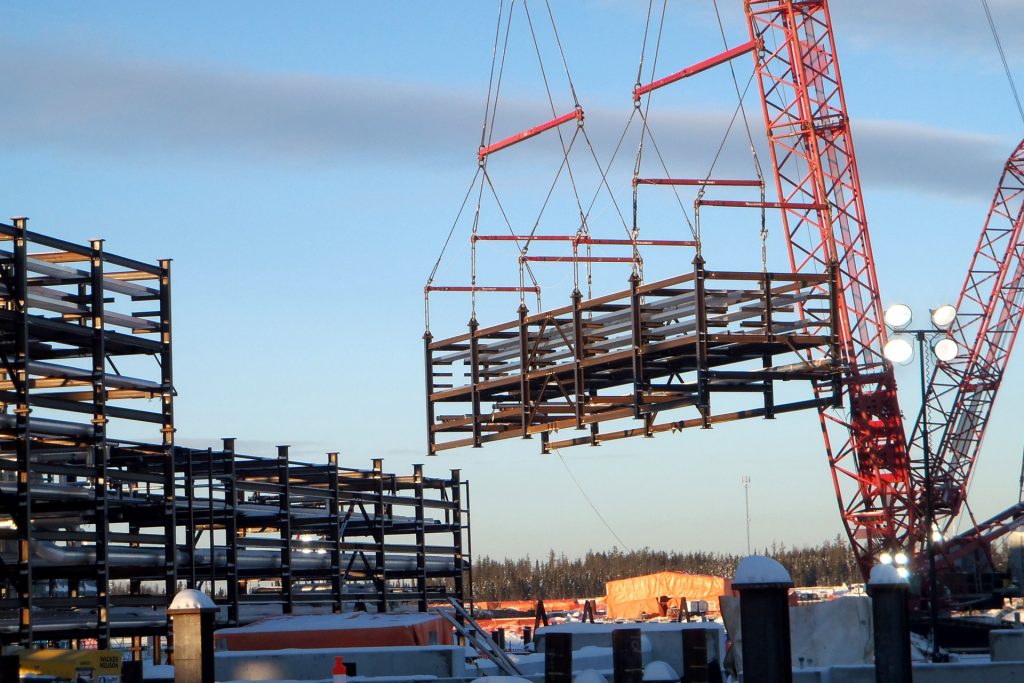 A crane lifts structural steel at a building side